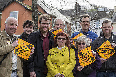 A group of Lib Dem campaigners in a line, with some holding orange diamond posters.